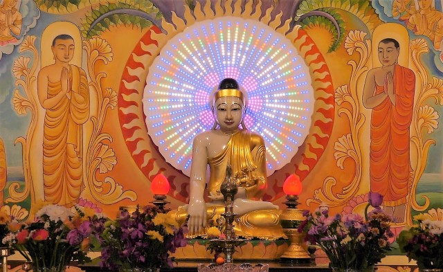 The Buddha image emits rays in the form of various patterns and symbols radiates in various colours includes the swastika symbol in gold (yellow). 